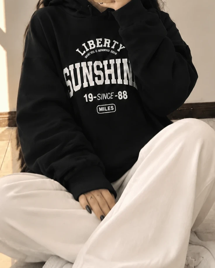 تن‌خور هودی مشکی دخترانه SUNSHINE در حالت نشسته روی زمین با چاپ سفید LIBERTY گیلمد